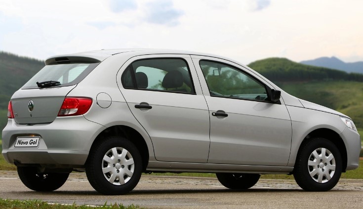 Foto mostrando a traseira e a diagonal direita de um VW Gol 2012 prateado que está estacionado em uma rua de asfalto.