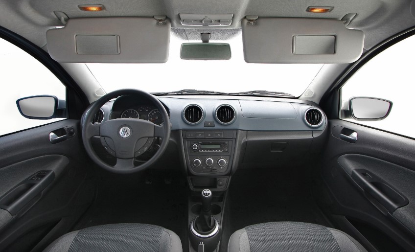 Foto mostrando o painel do carro. É possível ver o volante, as saídas e os comandos de ar e do rádio, o porta-luvas, a lateral as portas e os assentos dos bancos dianteiros.
